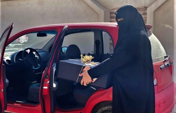 Malika with the rented car she uses for her delivery and sweets-making business.