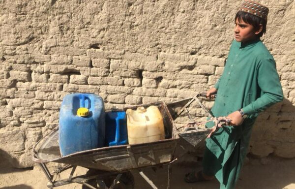 A boy is carrying water tanks in a wheel barrow on his way to collect clean water for his family.