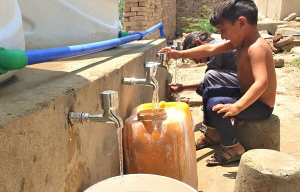 A couple of children laughing and playing while collecting clean water from the collection point rehabilitated by Cesvi in the village.