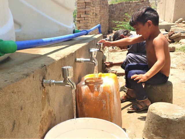 A couple of children laughing and playing while collecting clean water from the collection point rehabilitated by Cesvi in the village.