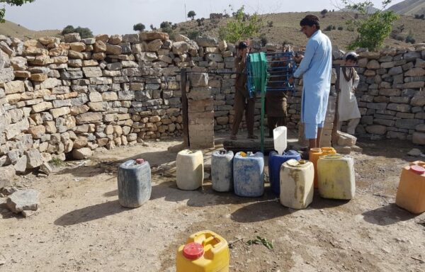 A group of men and boys is collecting water from an open dug well.